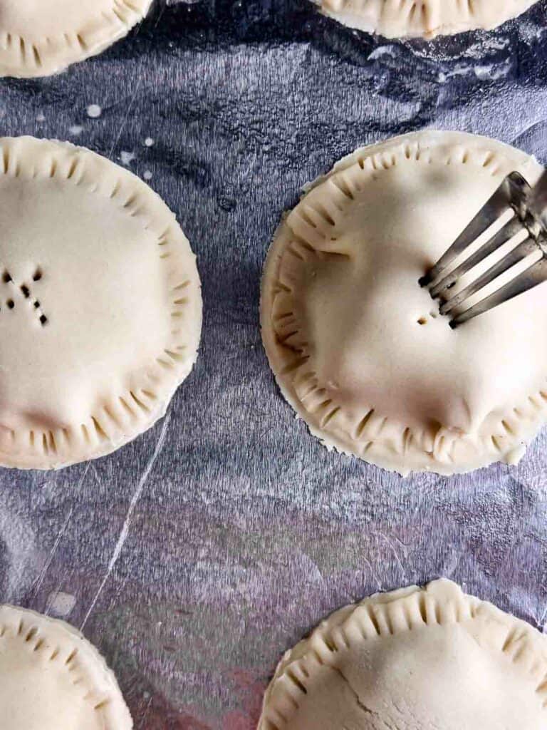 Poking holes into mini apple pies to release steam.