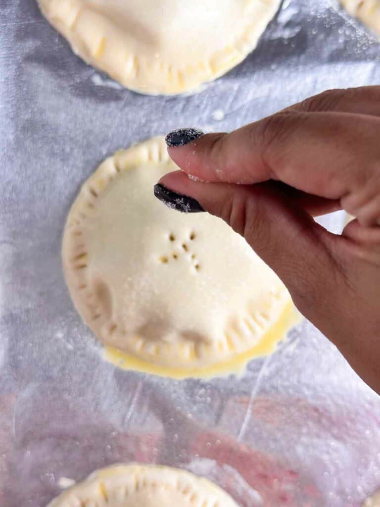 Sprinkling sugar on top of mini apple pies.