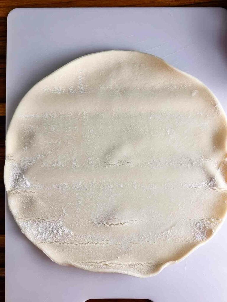 Unrolled pie crust on a white cutting board.