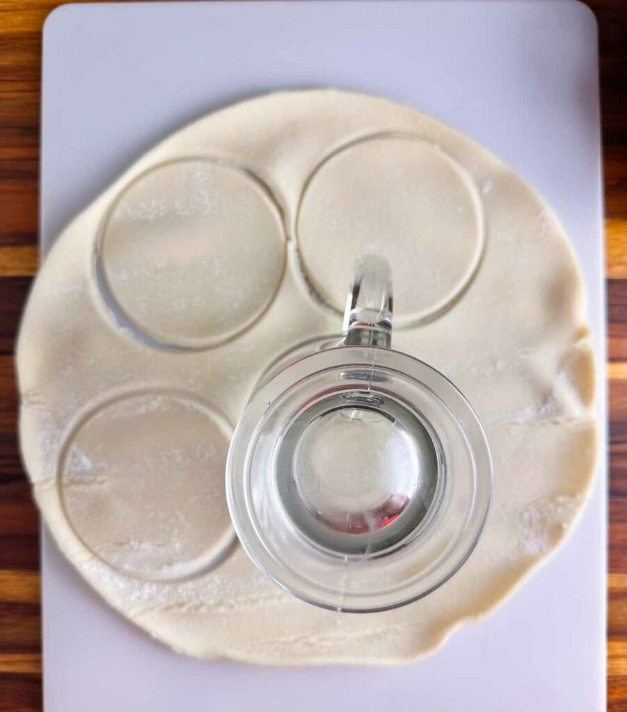 using a round mug to cut out mini apple pie crusts.