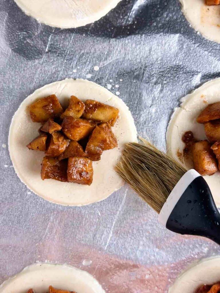 Brushing water on the sides of a mini apple pie.