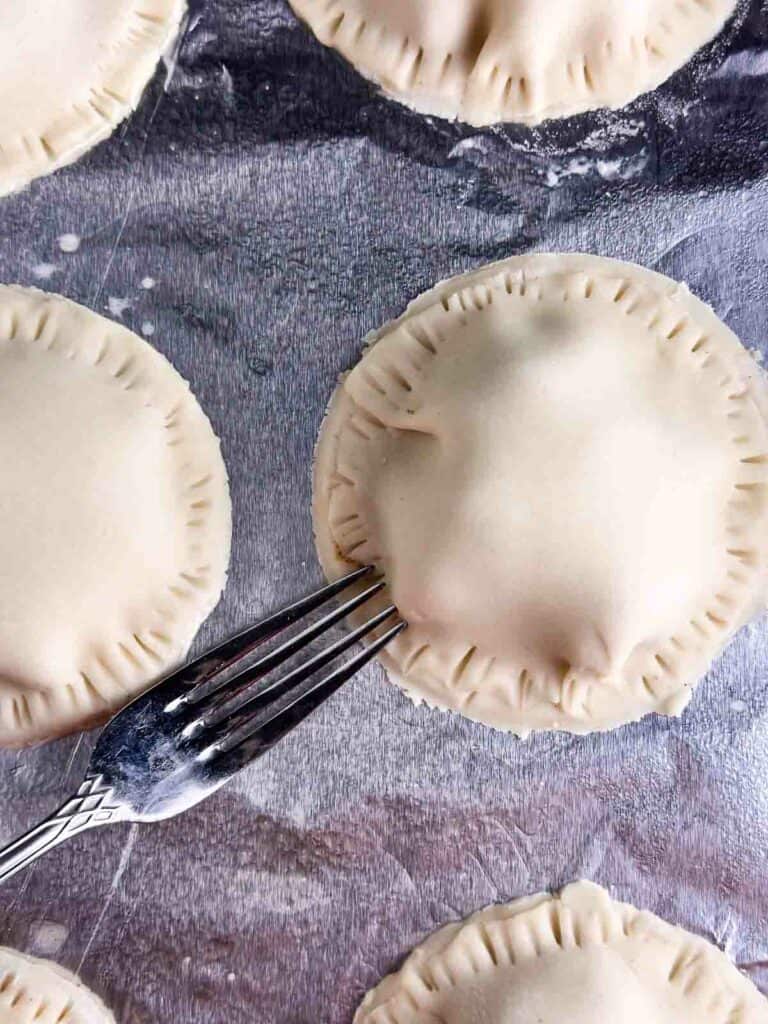 Using a fork to push the apple pie crusts together.