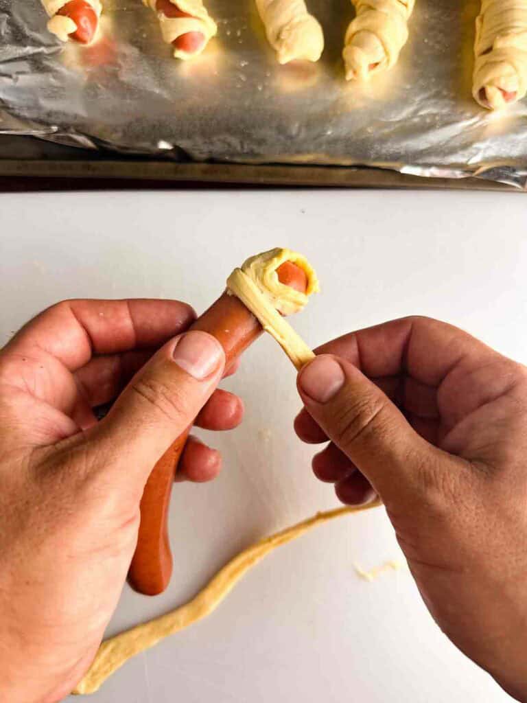 Wrapping a hot dog with crescent roll strips to create mummy hot dogs.