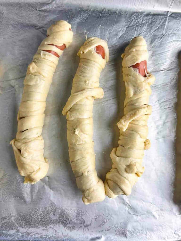 Fully wrapped hot dogs on a baking sheet.