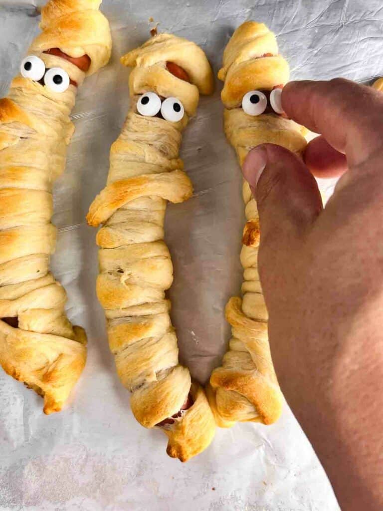 Adding eye balls to mummy hot dogs.