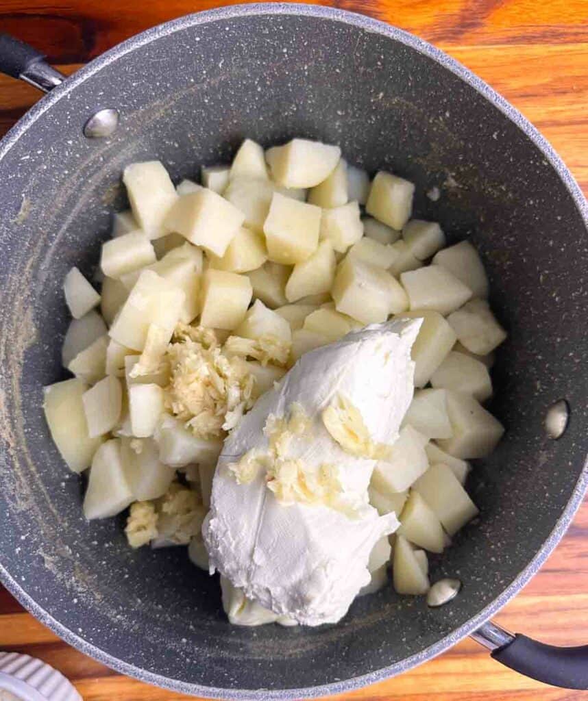 Cooked potatoes, cream cheese, and garlic ready to mash together.