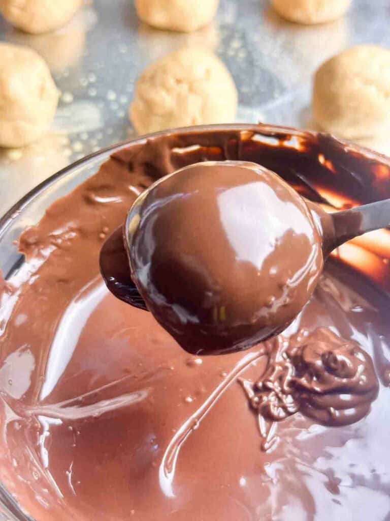 Dipping a peanut ball in melted chocolate.
