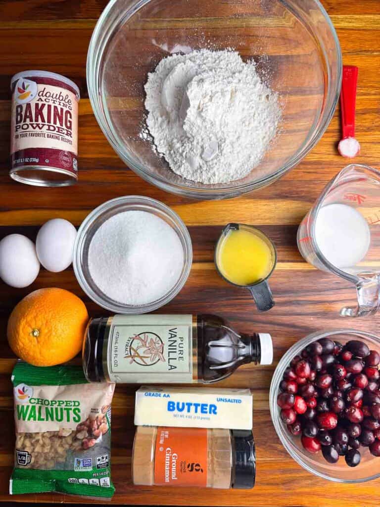Ingredients for cranberry orange bread with walnuts: baking powder, flour, salt, eggs, sugar, orange juice, milk, orange zest, vanilla extract, cranberries, walnuts, butter, and cinnamon.