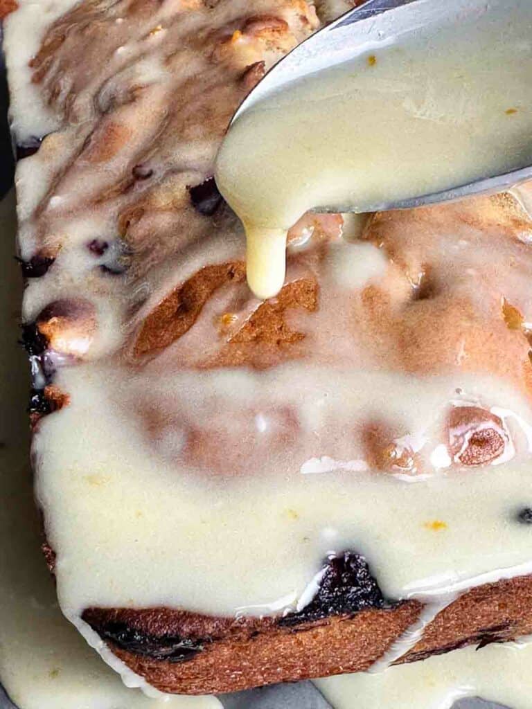 Adding glaze to cranberry orange bread with walnuts.