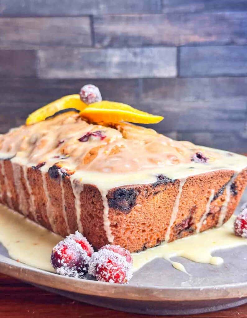 Cranberry orange bread with walnuts on a serving plate with a glaze with orange slices and cranberries.