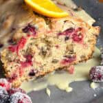 Cranberry orange bread with walnuts on a serving tray with cranberries and orange slices.