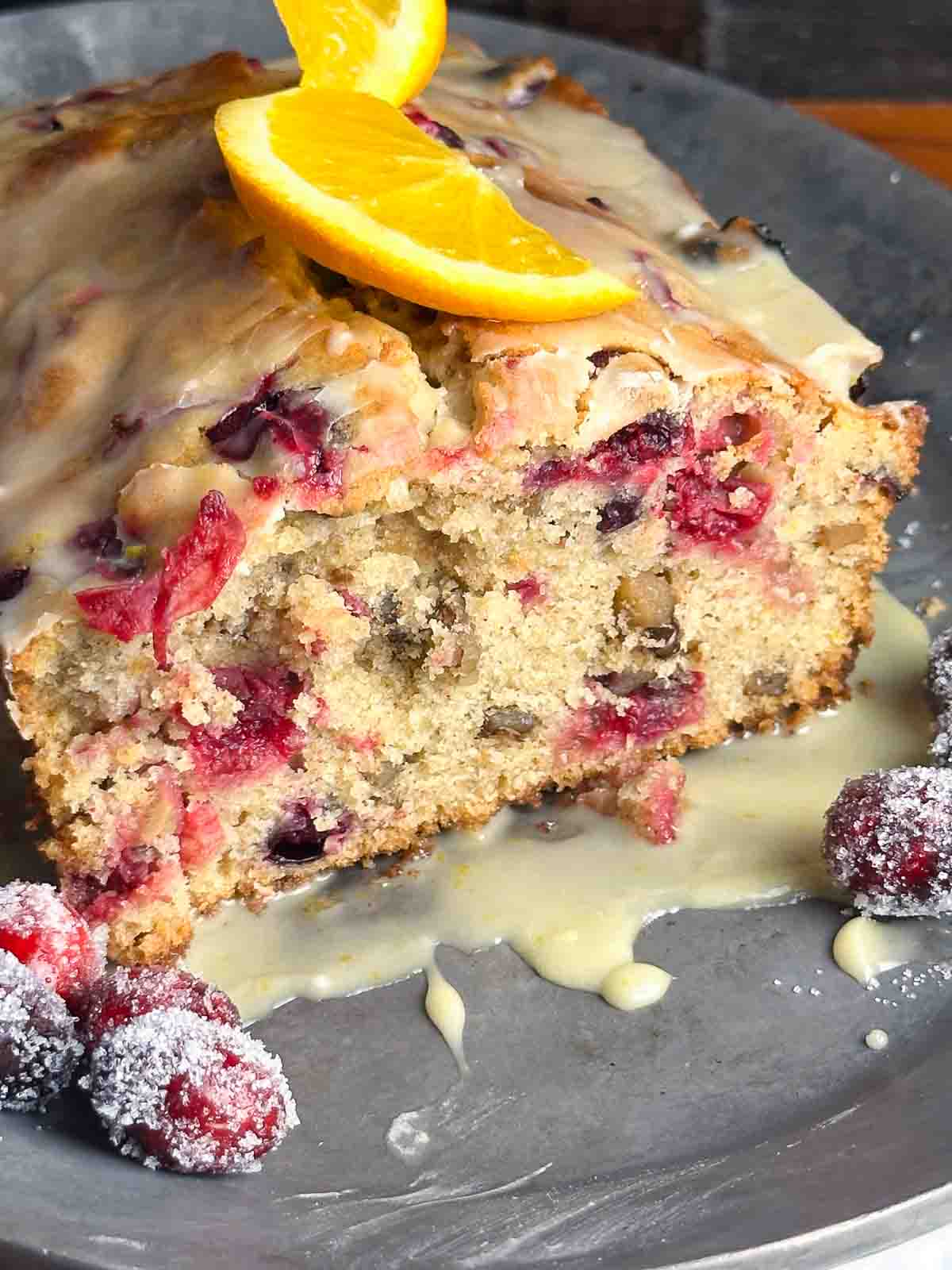 Cranberry orange bread with walnuts on a serving tray with cranberries and orange slices.