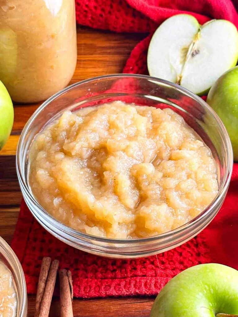 2 bowls and a mason jar of homemade applesauce in glass bowls with apples