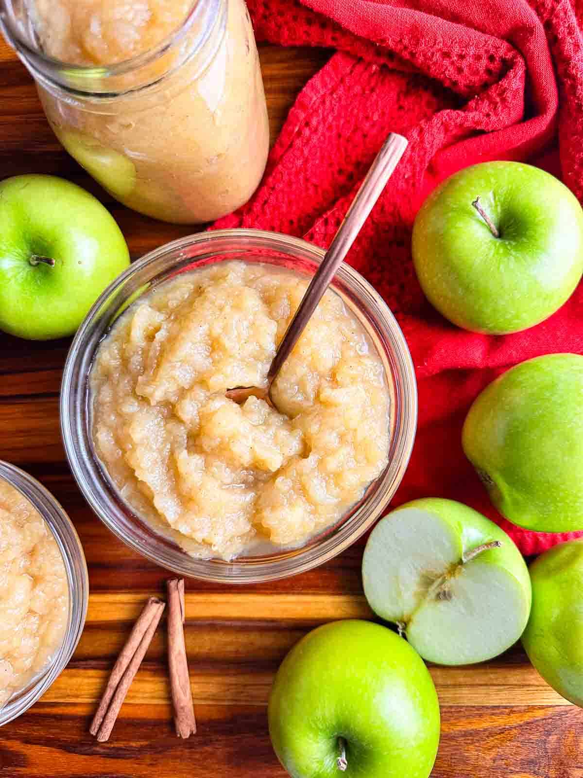2 bowls and a mason jar of homemade applesauce in glass bowls with apples