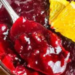 Orange cranberry sauce with a spoon and orange slice.