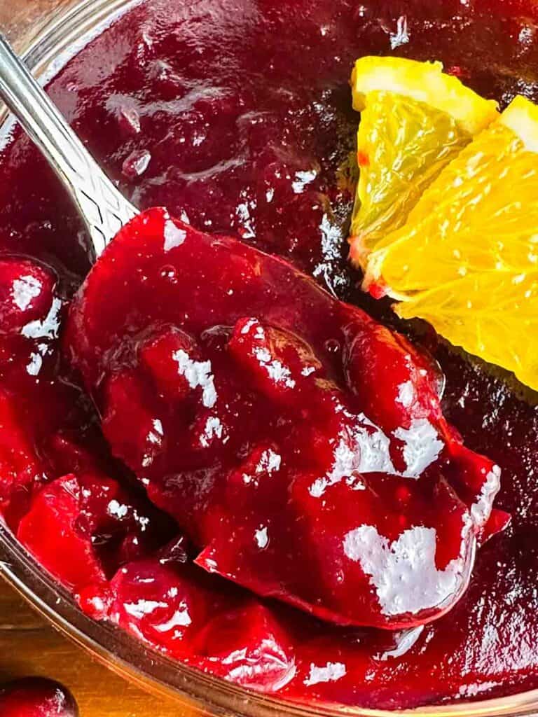 Orange cranberry sauce with a spoon and orange slice.