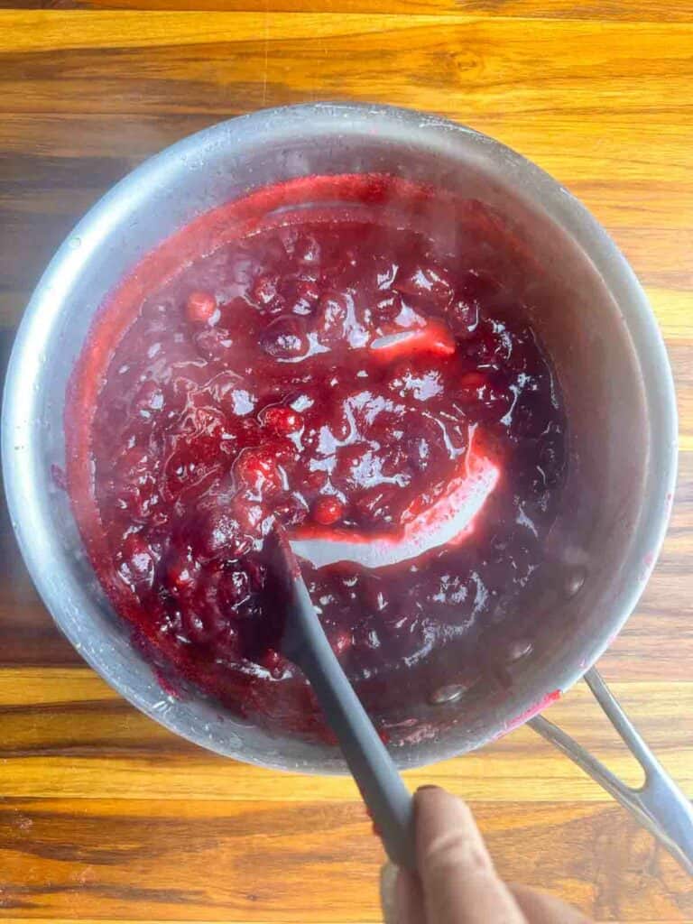 Hot orange cranberry sauce shown in a pot and how it slowly refills an opening.