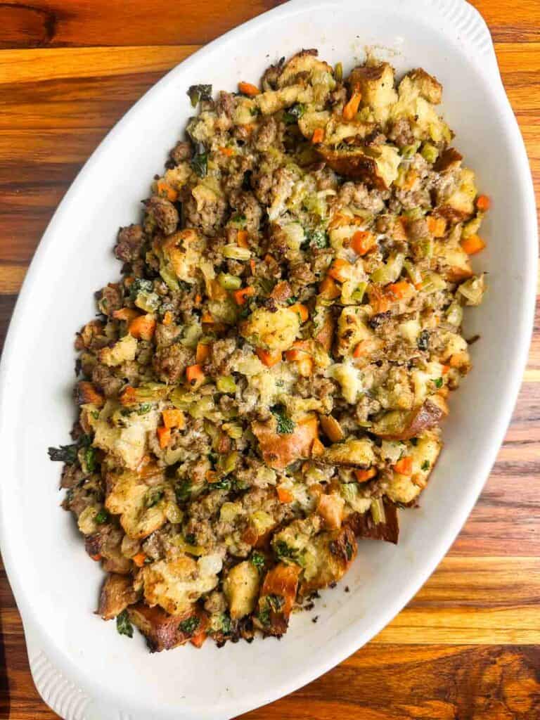 Sausage stuffing in a white baking dish on a wood counter.