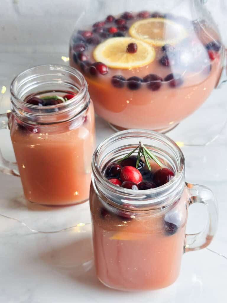 Christmas punch with cranberries and rosemary in mason jars and a pitcher.