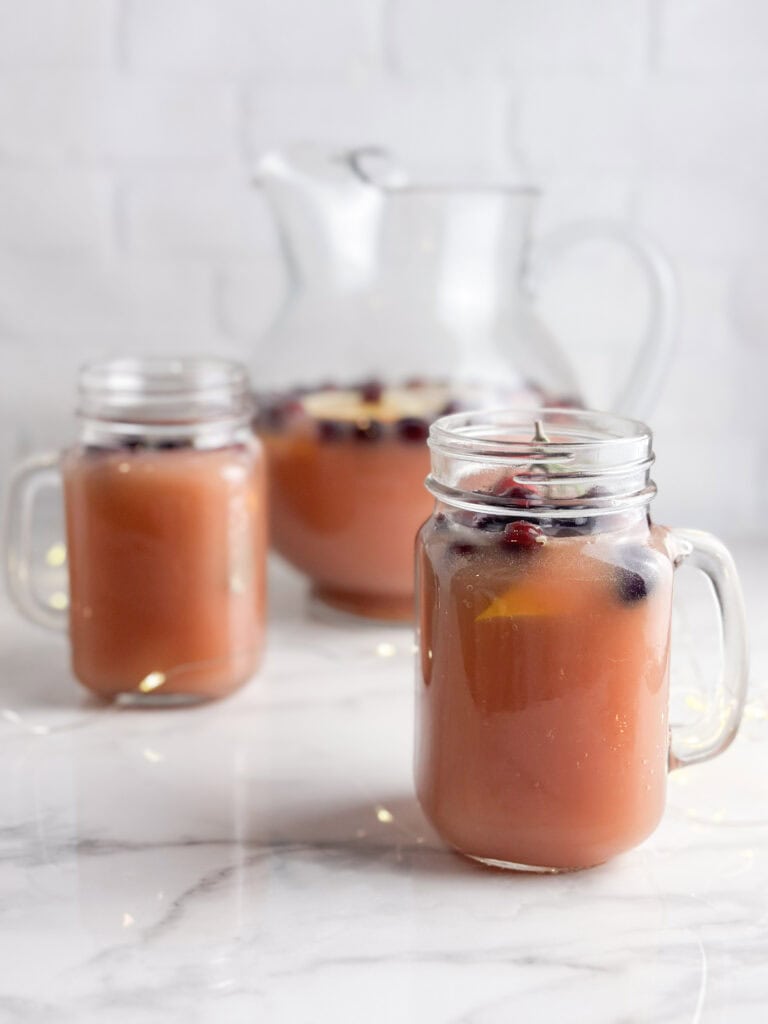 Christmas punch with cranberries and rosemary in mason jars and a pitcher.