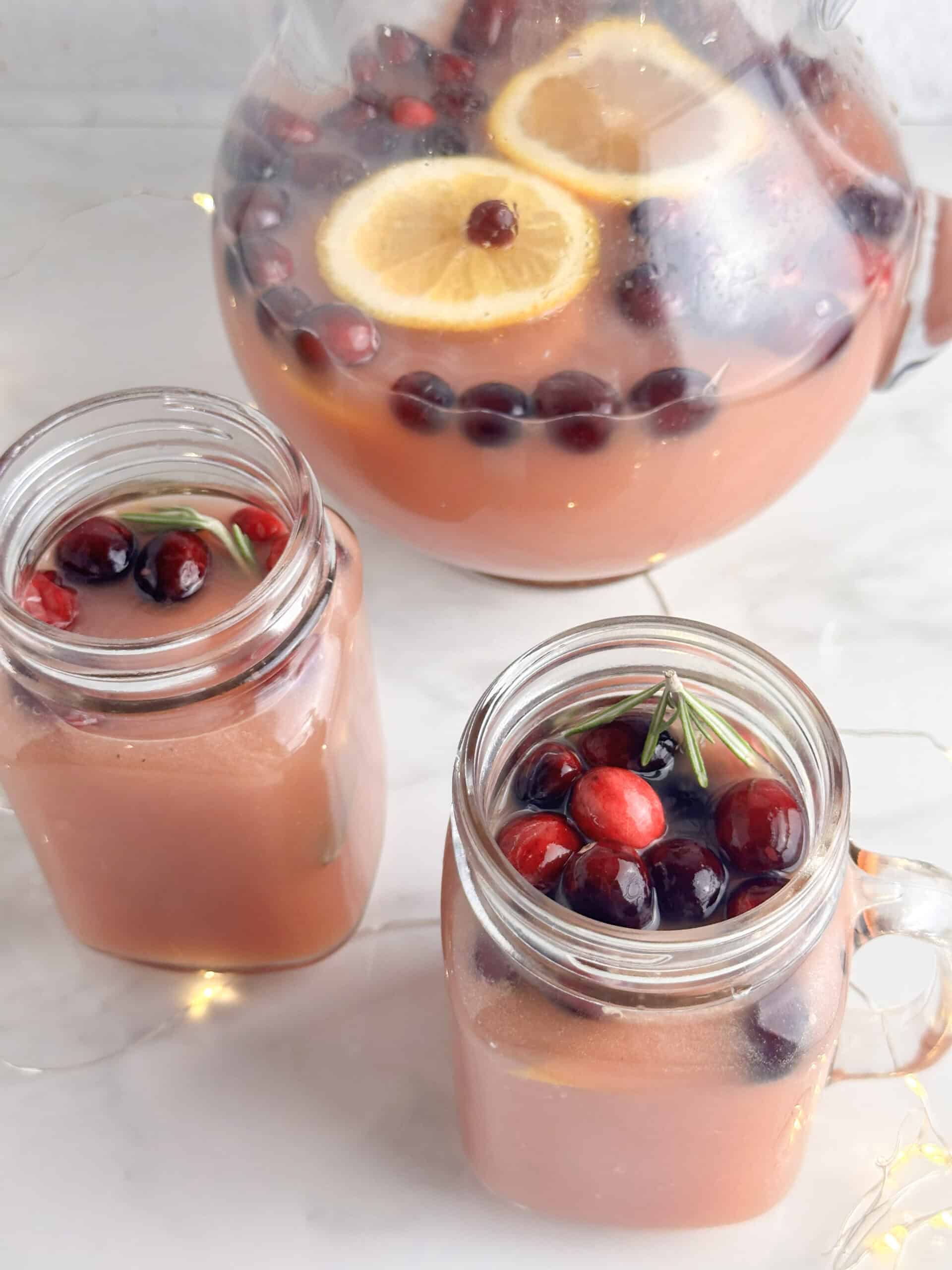 Christmas punch with cranberries and rosemary in mason jars and a pitcher.