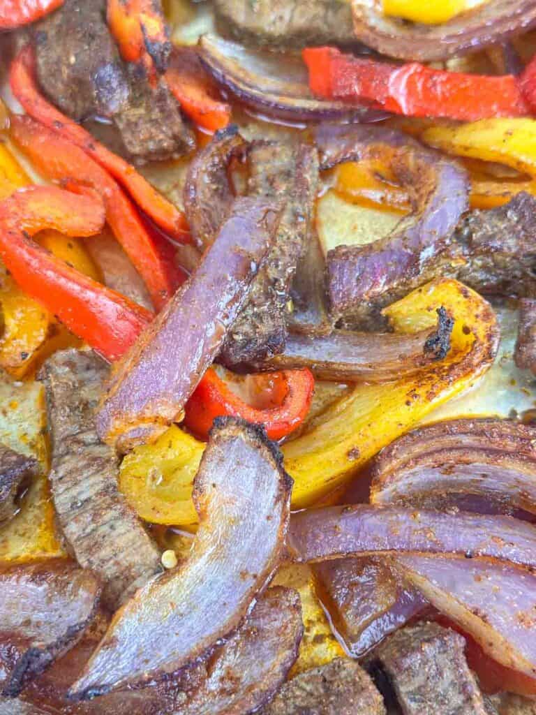 Close up of cooked sheet pan steak fajitas with onions and peppers.