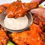 Tray of homemade buffalo chicken wings with celery, carrots, and blue cheese. Image shows dipping wing in blue cheese.