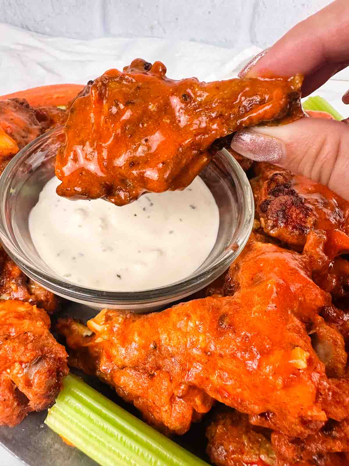 Tray of homemade buffalo chicken wings with celery, carrots, and blue cheese. Image shows dipping wing in blue cheese.