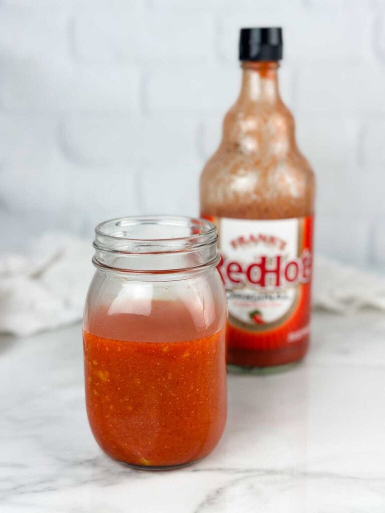 Jar of homemade buffalo wing sauce in front of Frank's Red Hot.