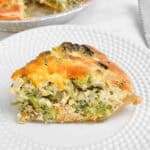 Serving broccoli quiche on a white plate with rest in the background.