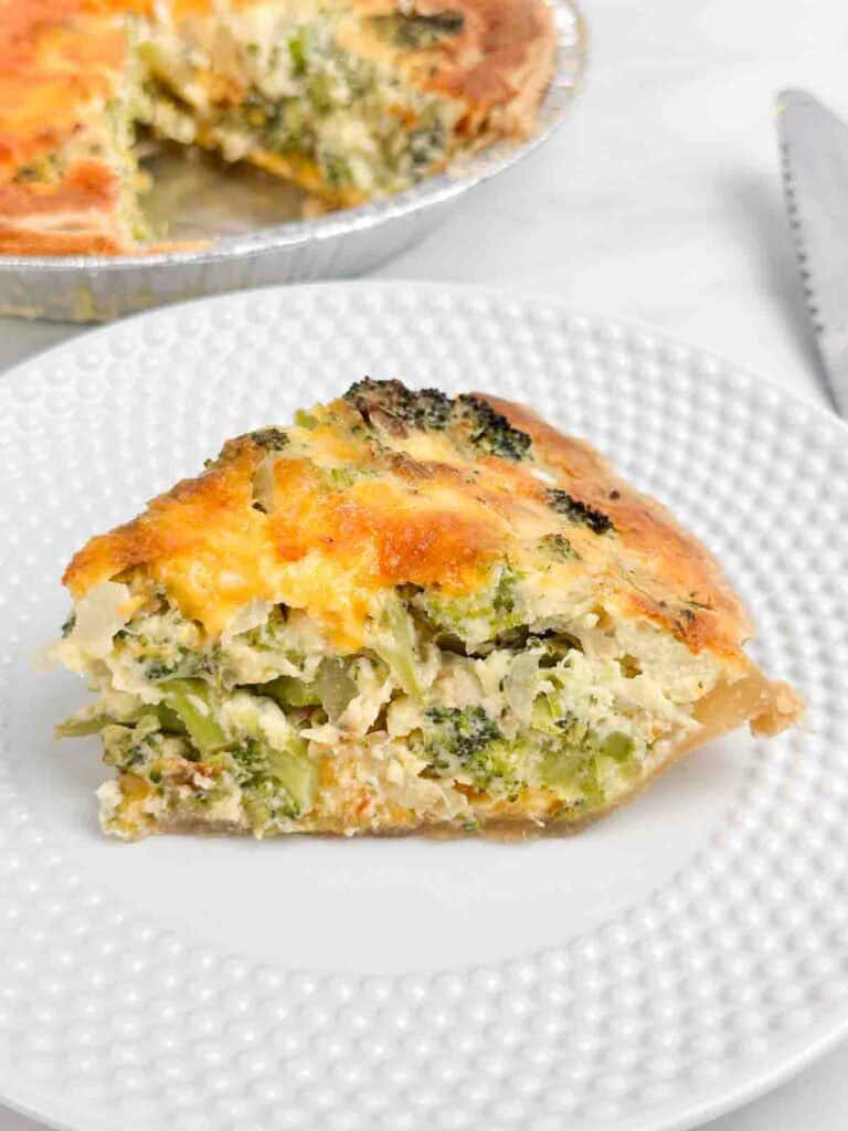 Serving broccoli quiche on a white plate with rest in the background.