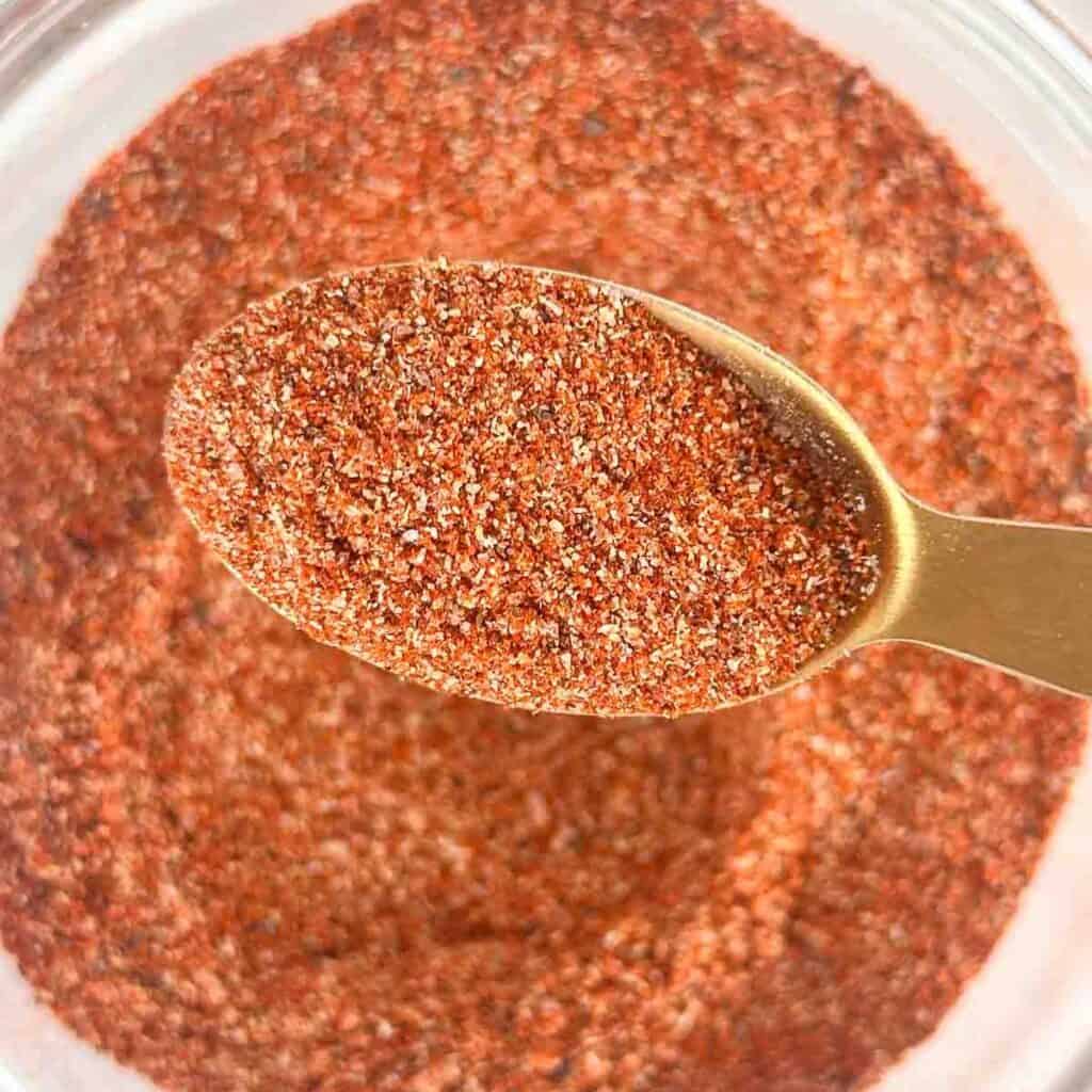 Jar of homemade burger seasoning with a burger in the back made with it.