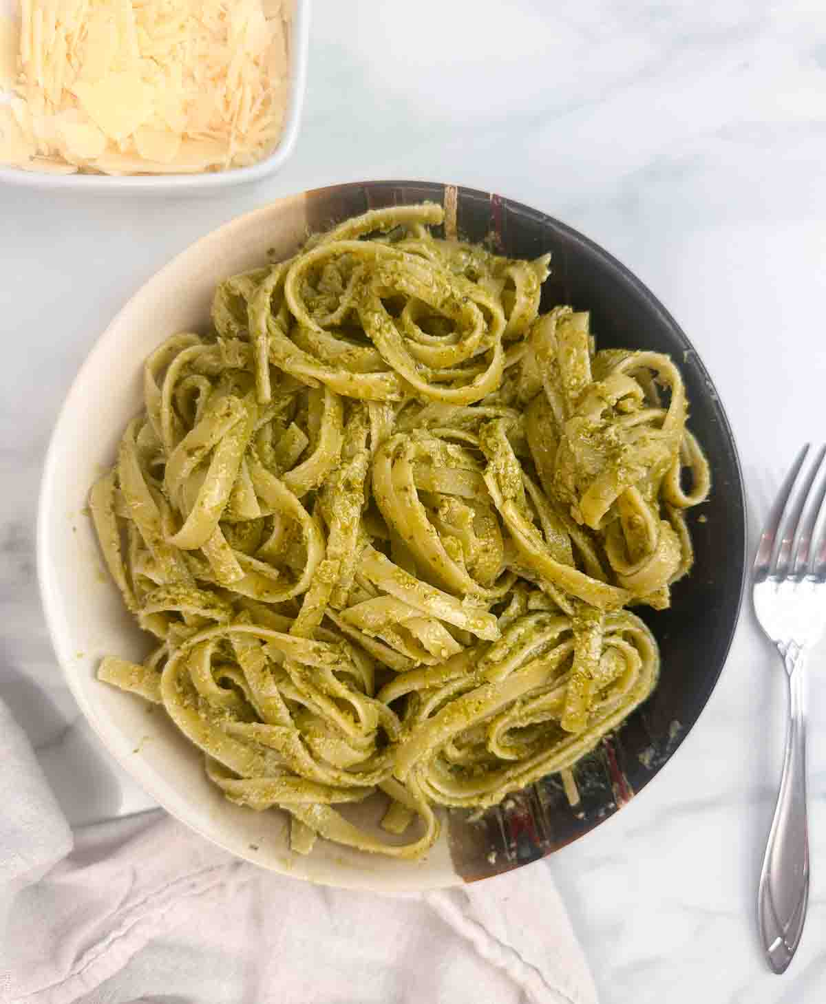 A bowl of pasta with creamy pesto sauce with parmesan cheese.