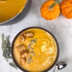 Creamy pumpkin soup with a swirl of cream, croutons, and pumpkin seeds on top.