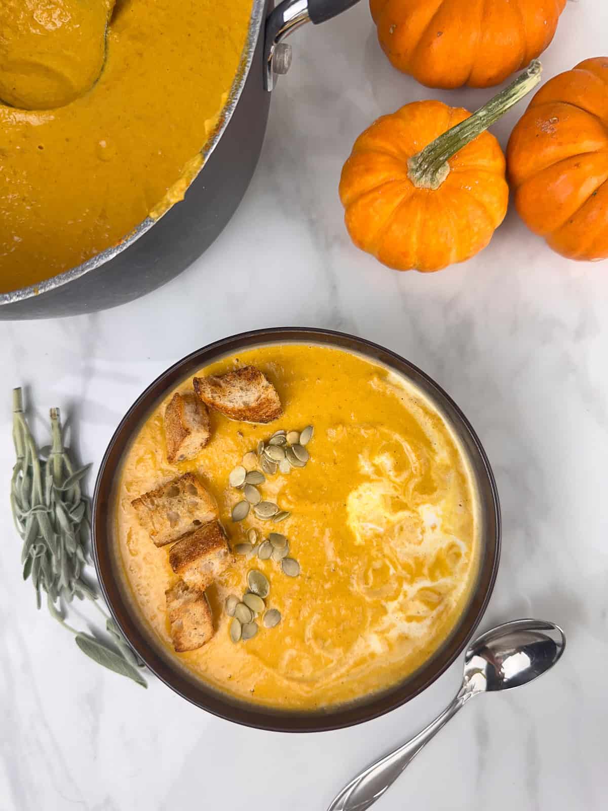 Creamy pumpkin soup with a swirl of cream, croutons, and pumpkin seeds on top.