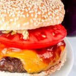 BBQ burger shown with tomatoes, red onions, and lettuce on a seeded bun.