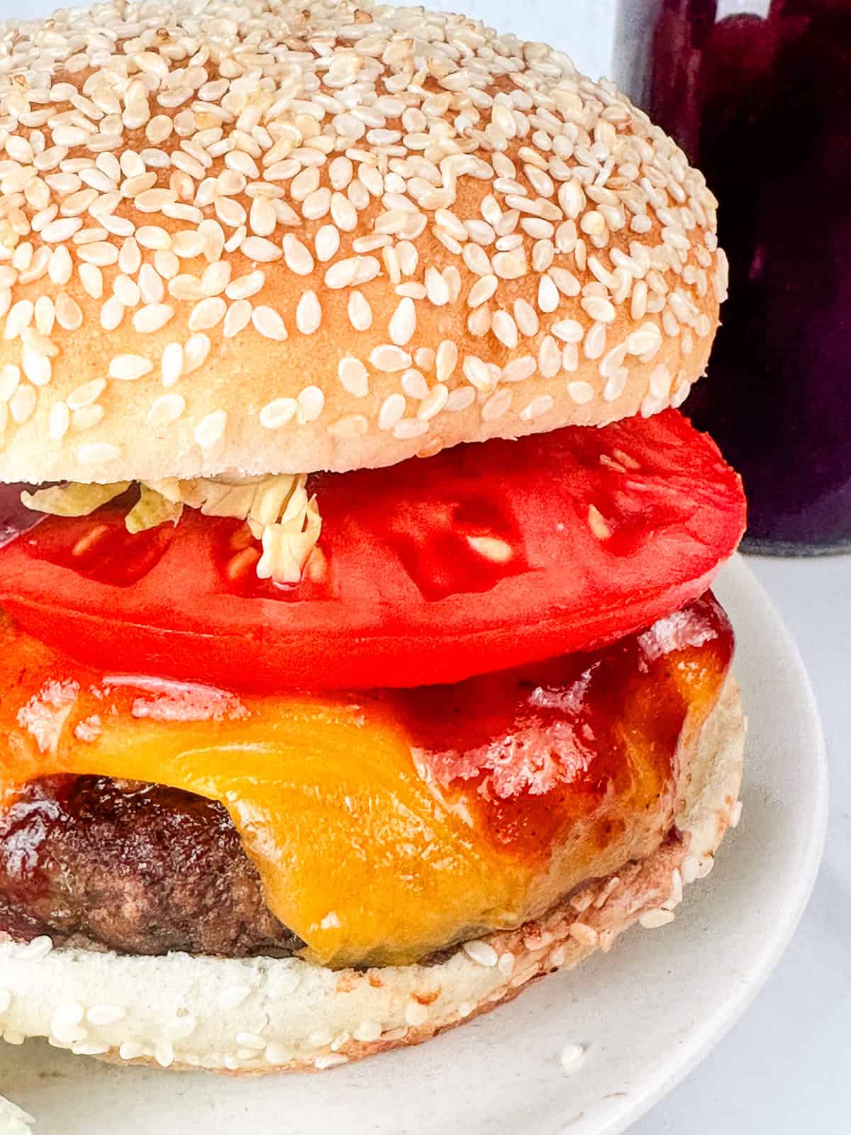 BBQ burger shown with tomatoes, red onions, and lettuce on a seeded bun.