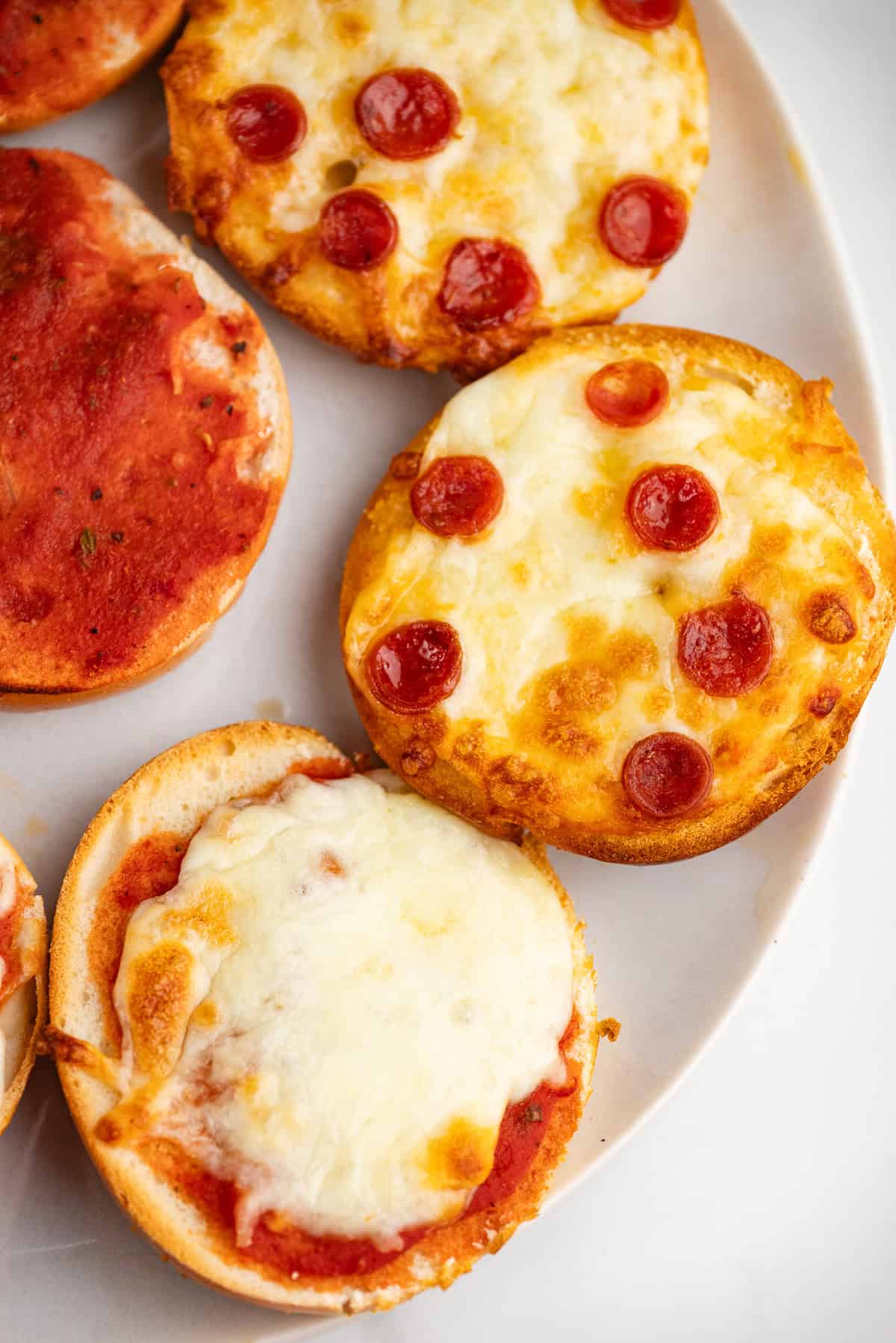 Close up of a mini pizza bagel with pepperoni and sauce on a white plate.