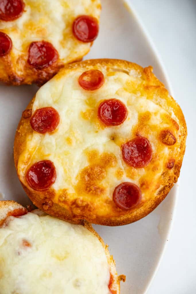 Close up of a mini pizza bagel with pepperoni on a white plate.
