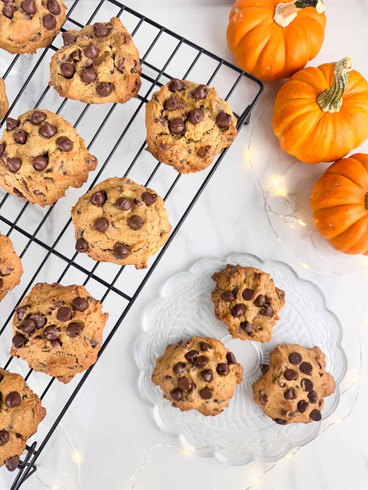 Pumpkin chocolate chip cookies cooling on a wire rack and served on a clear plate.